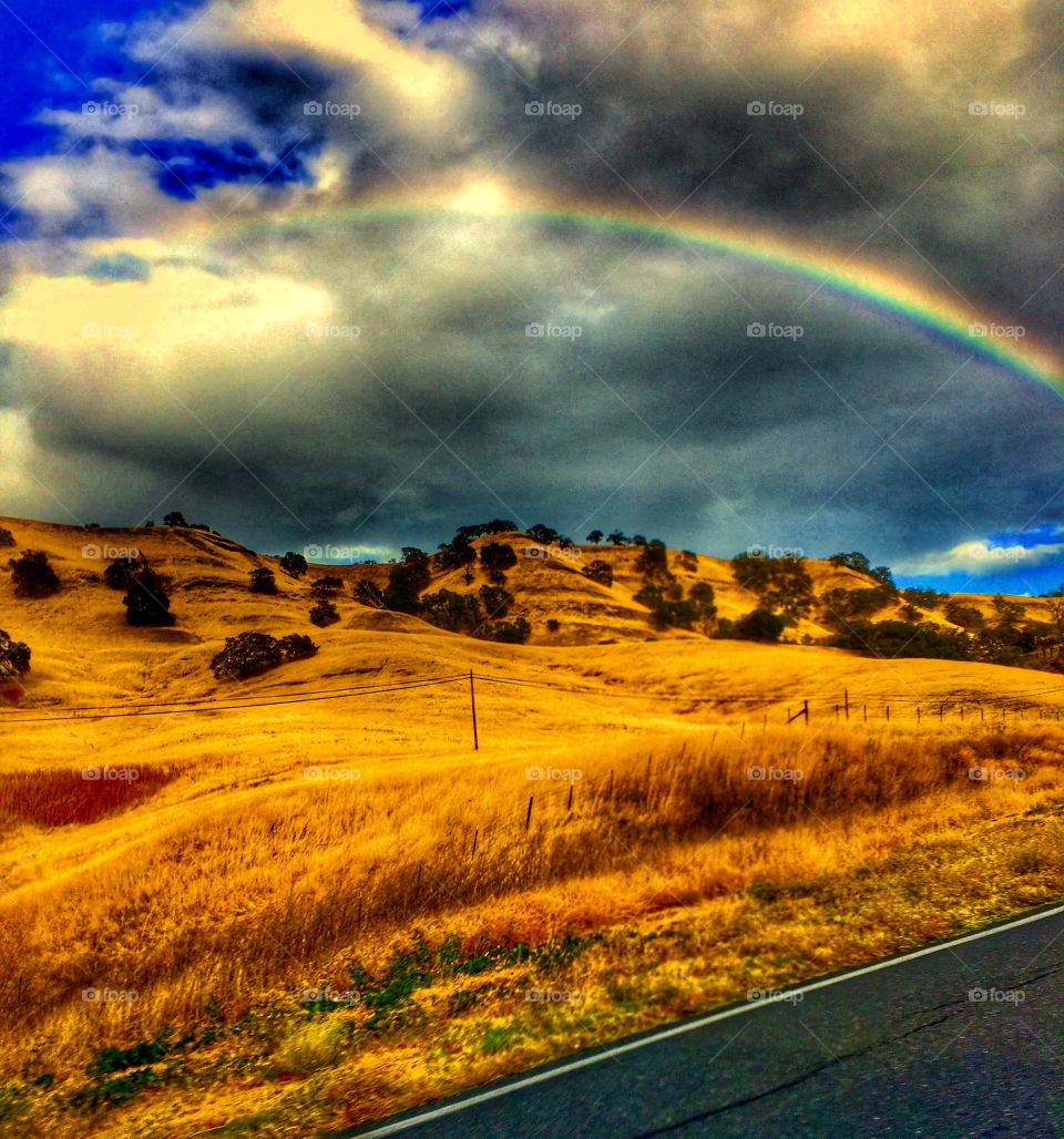 Storm clouds and a bright rainbow over the golden hills of California. 