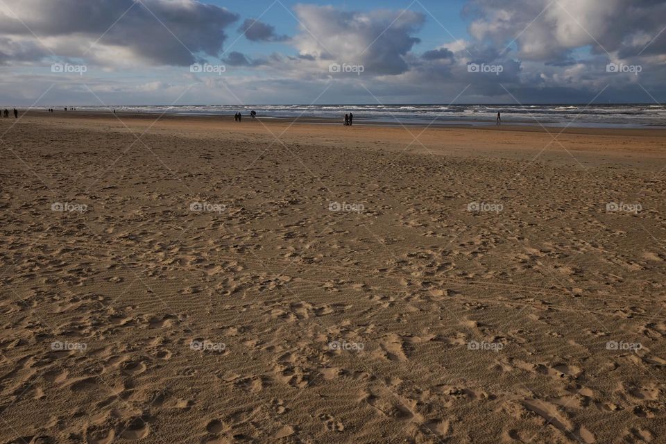 Sand space, area. Beach, sand and clouds on a lovely sunny winter day with clouds in the blue sky. People on the beach (in distance) 