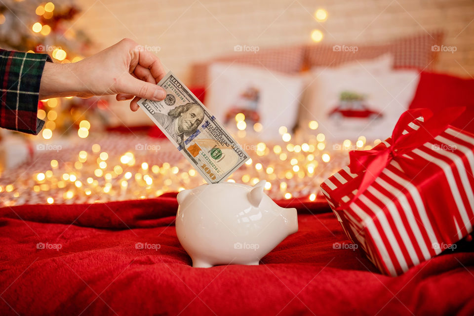 piggy bank with 100 dollars banknote in festive New Year atmosphere of scenery.  Magical bokeh with Christmas tree and bright lights.