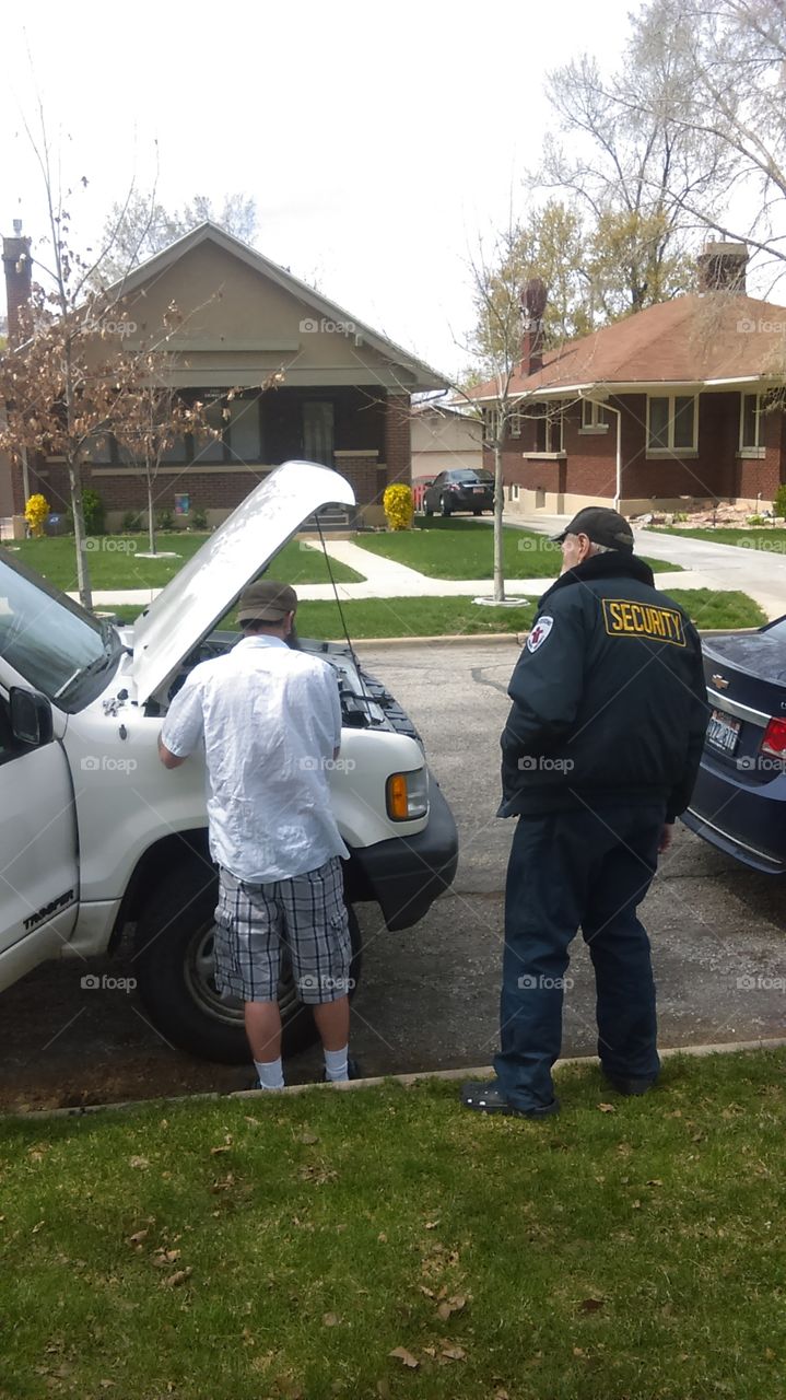 man fixing his car with a security guard