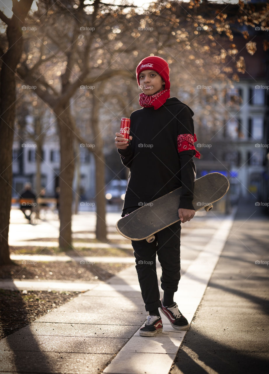 Teenager with a skateboard and Coca-Cola in his hands on the street