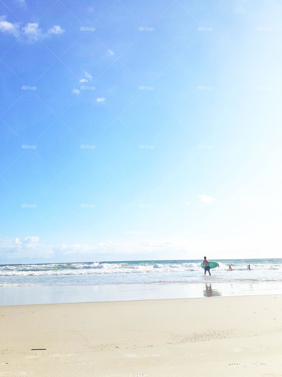 A surfer Carrie's a surfboard into the ocean for a day of surfing at Ponce Inlet Beach in Ponce Inlet Florida.