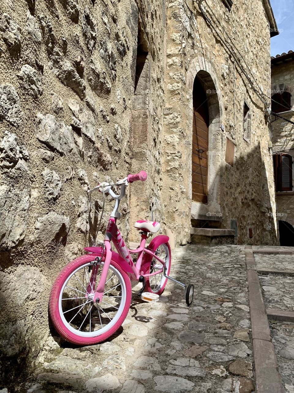 A pink children's bicycle leaning against the wall of an old house contrasts with the ancient world represented by the ancient town.