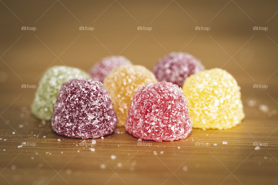 A portrait of multiple pieces of candy sprinkled with sugar on top of them on a wooden table.