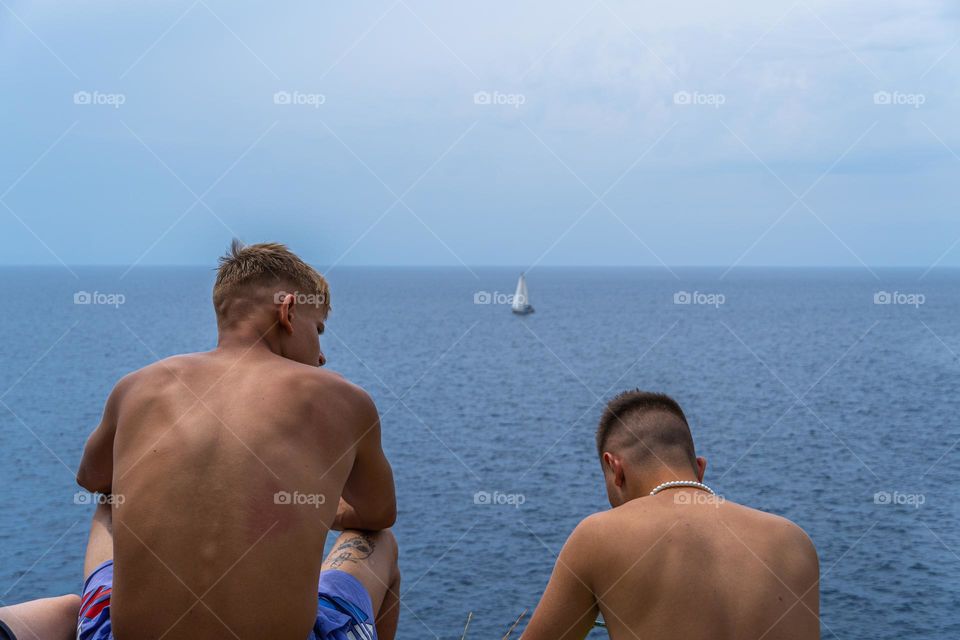Two boys sitting in focus in the background is lonely boat in endless horizon of water 