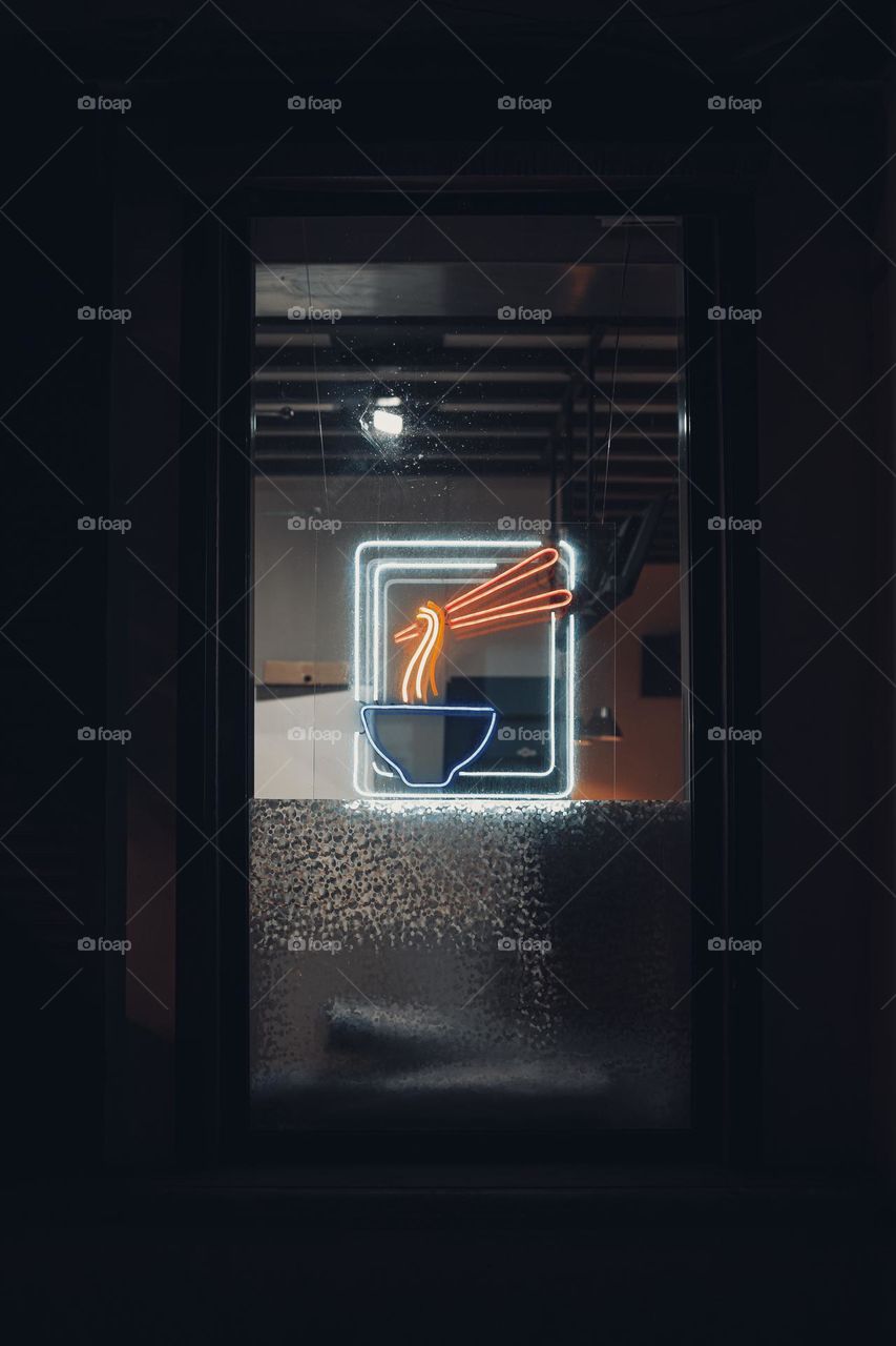 Neon sign on a dark background with bright bowl and noodles . Vertical shot.