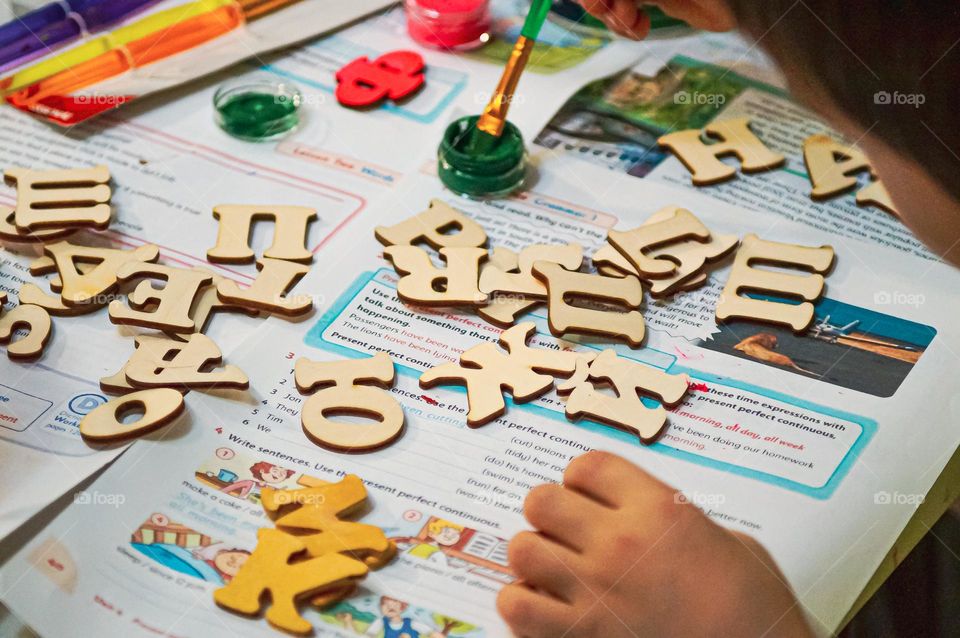 A boy with his mother paints wooden letters in different colors.