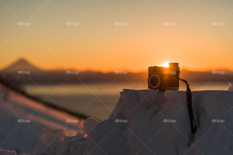 the camera stands on a snowdrift against the backdrop of the sunset