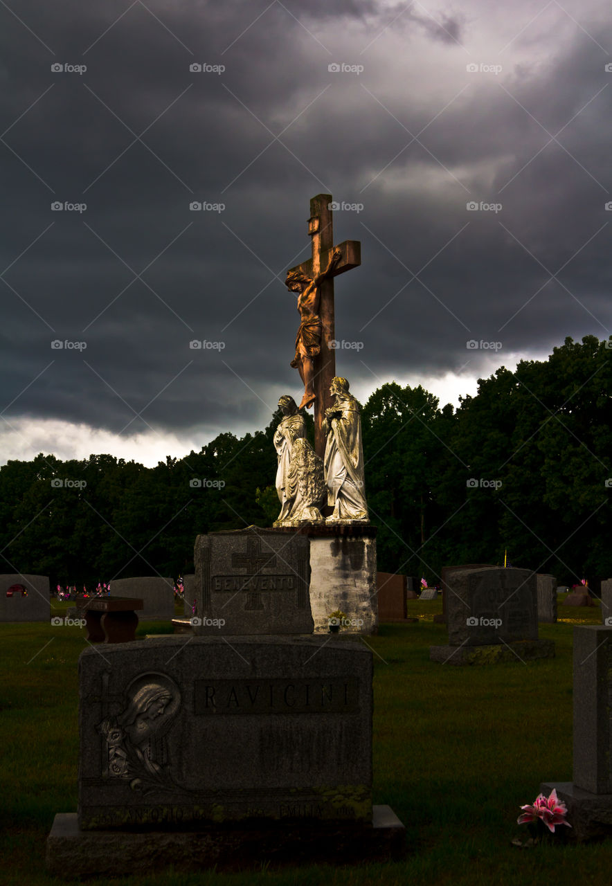 A large statue of Christ on the cross in a Cemetery on a cloudy stormy day. 