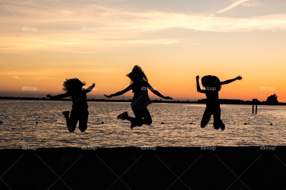 Three best friends jumping on the beach while the sunset is setting in