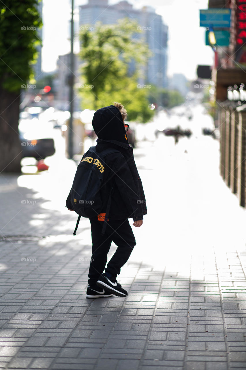 stylish boy in black clothes and glasses is walking along the street.  baby five years old, beautiful blond