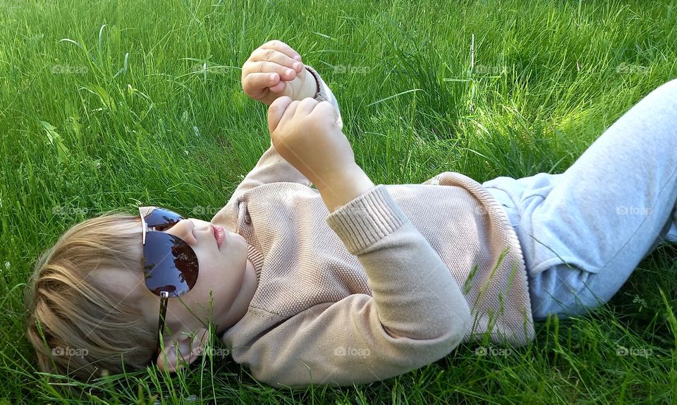 little boy wearing sunglasses is lying on the  grass