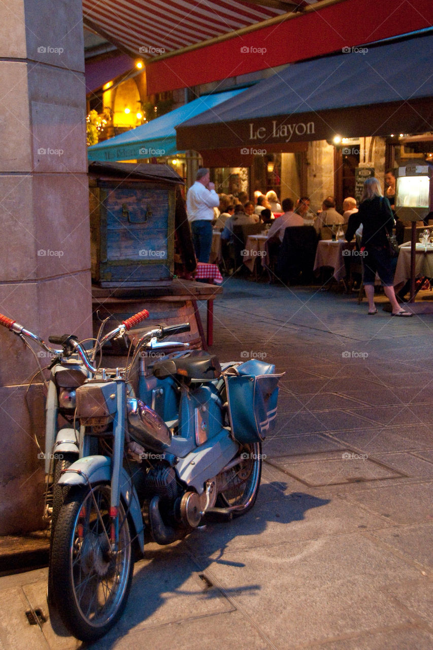 A moped leaned up against the wall at a outdoor dining Café in France