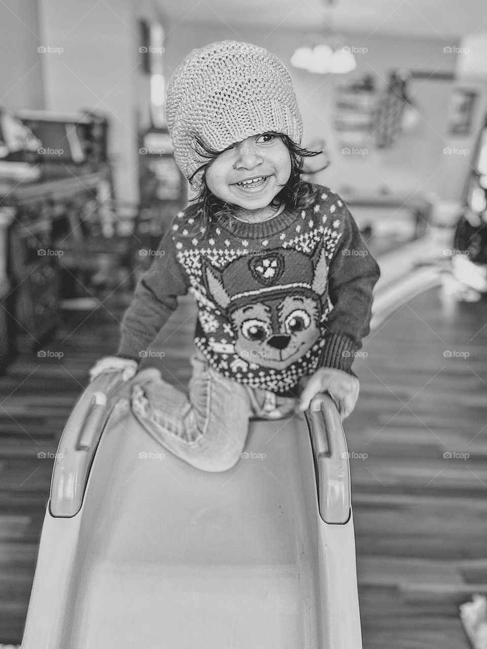 Toddler girl goes down indoor slide, winter time indoor fun, physical activity indoors during the winter, cute toddler smiling, keep one eye open, sliding indoors, having fun on a slide, toddler playing with slide, monochrome portrait of a child
