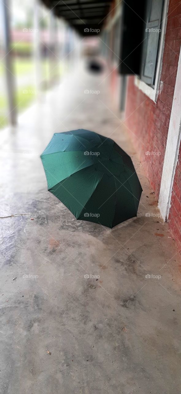 green umbrella on the floor of veranda...painted red brick wall..white washed pillar...cemented floor