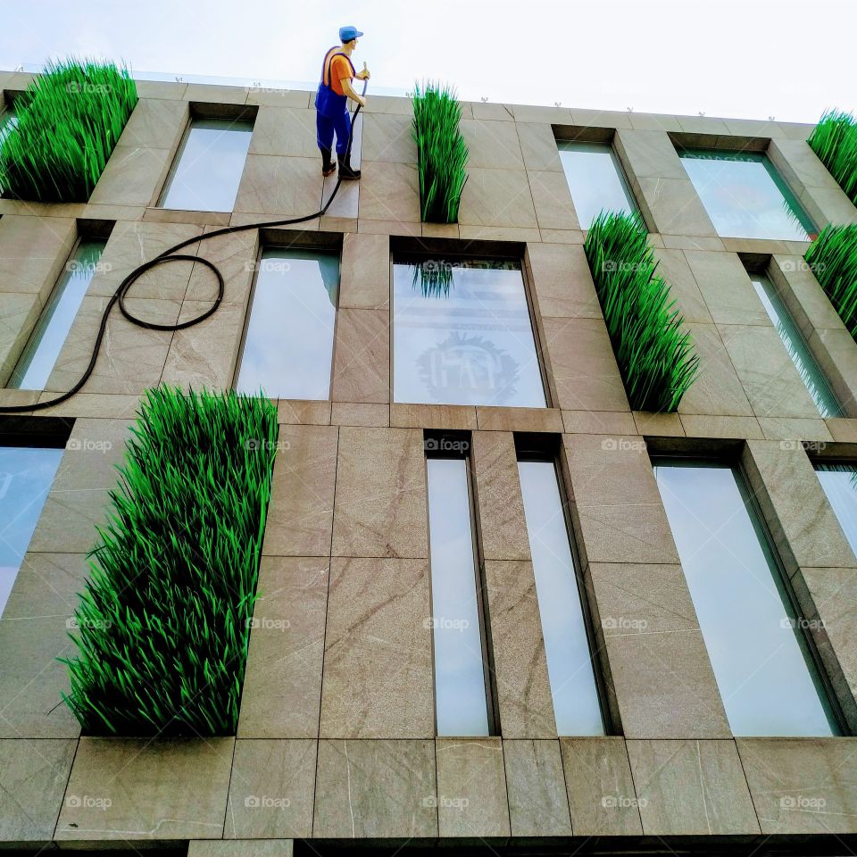 high-rise building facade, worker watering green grass