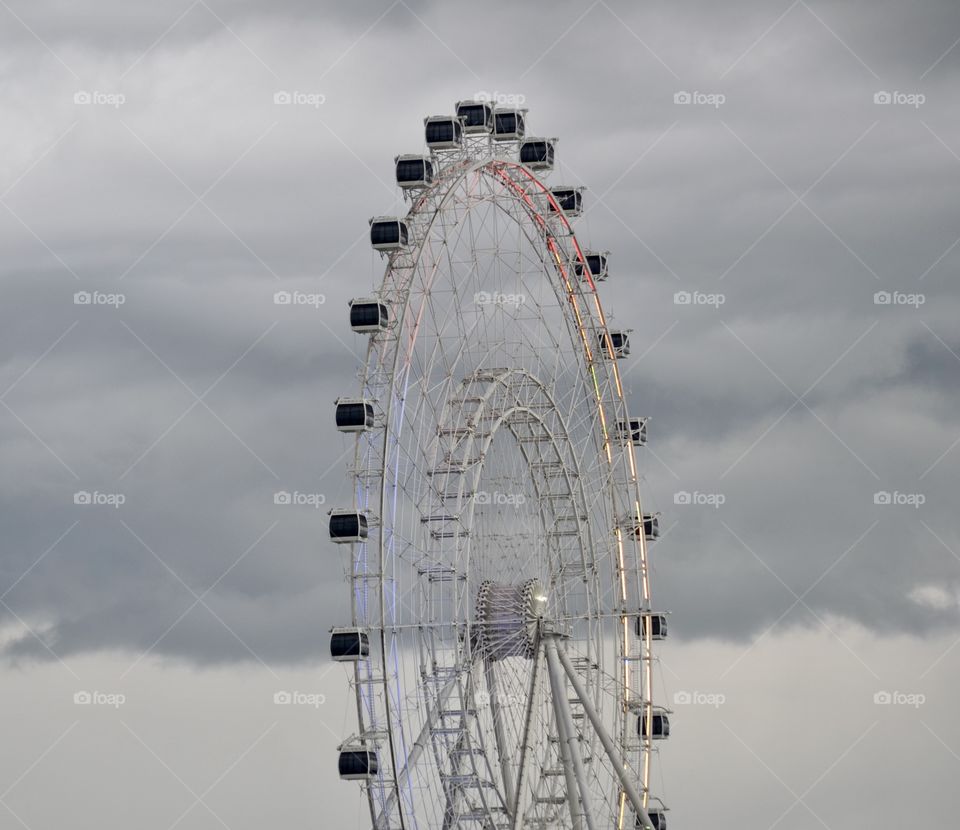 A tall Ferris wheel standing in front of a dark grey cloudy stormy sky