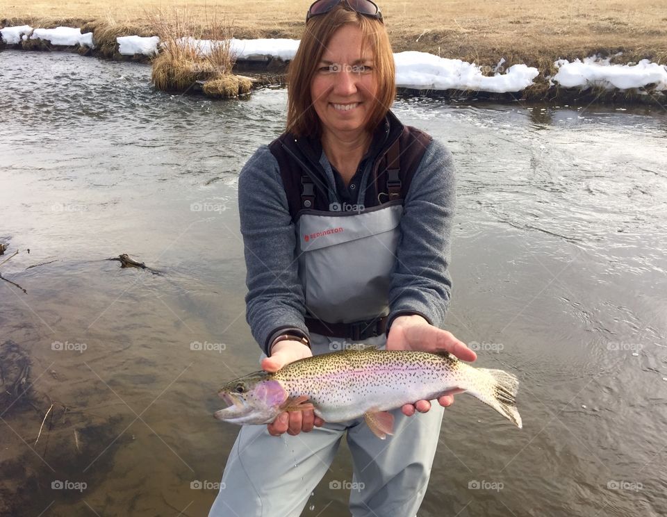 Lady holding rainbow trout in stream
