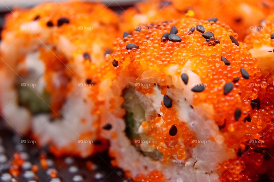 Bright tasty sushi with a large plan. Tuna meat sushi with green cucumber, sprinkled with sesame seeds and bright balls imitating red caviar