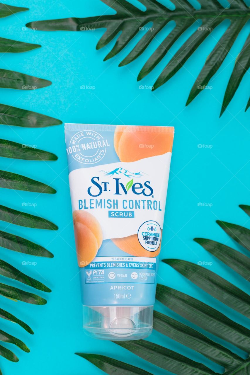 One tube natural apricot body scrub brand st. Ives lies on a blue background in the center with three palm branches on the edges, flat lay close-up. The concept of female cosmetics, body care, beauty.