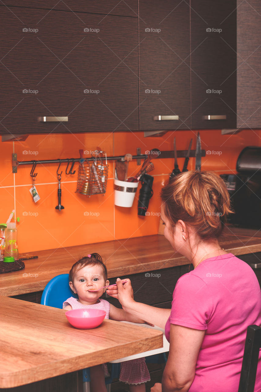 Woman feeding her daughter. Woman feeding her little girl in kitchen