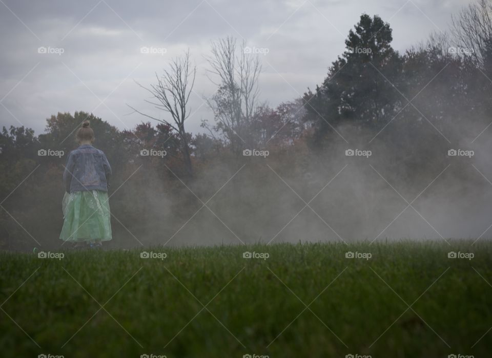 The Princess amongst the fog; Little girl in princess costume and jean jacket standing on foggy hill