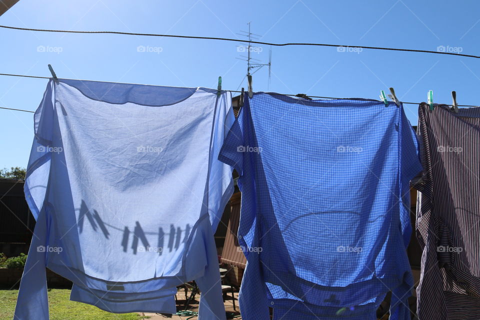 Two shirts hung up to dry on clothesline’s on sunny day, shadows of clothes pegs clothespins on shirts