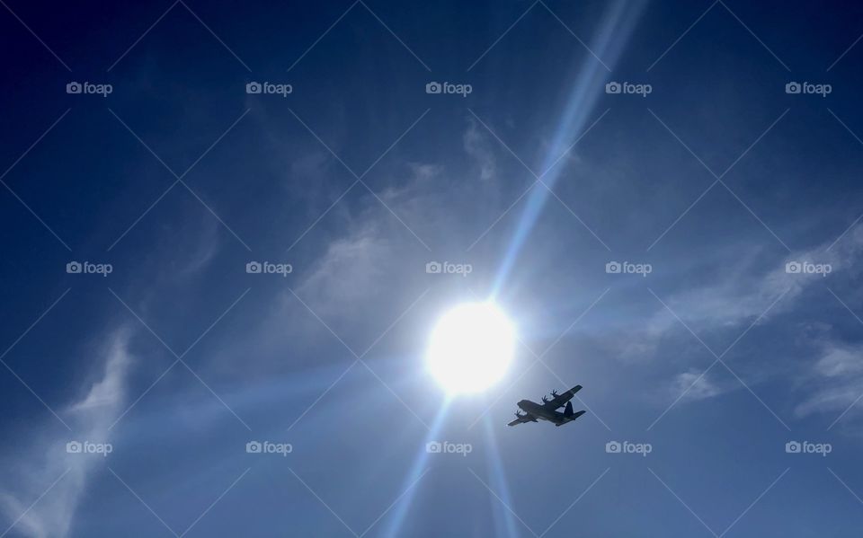 Military transport plane passing directly overhead at beach on sunny day 