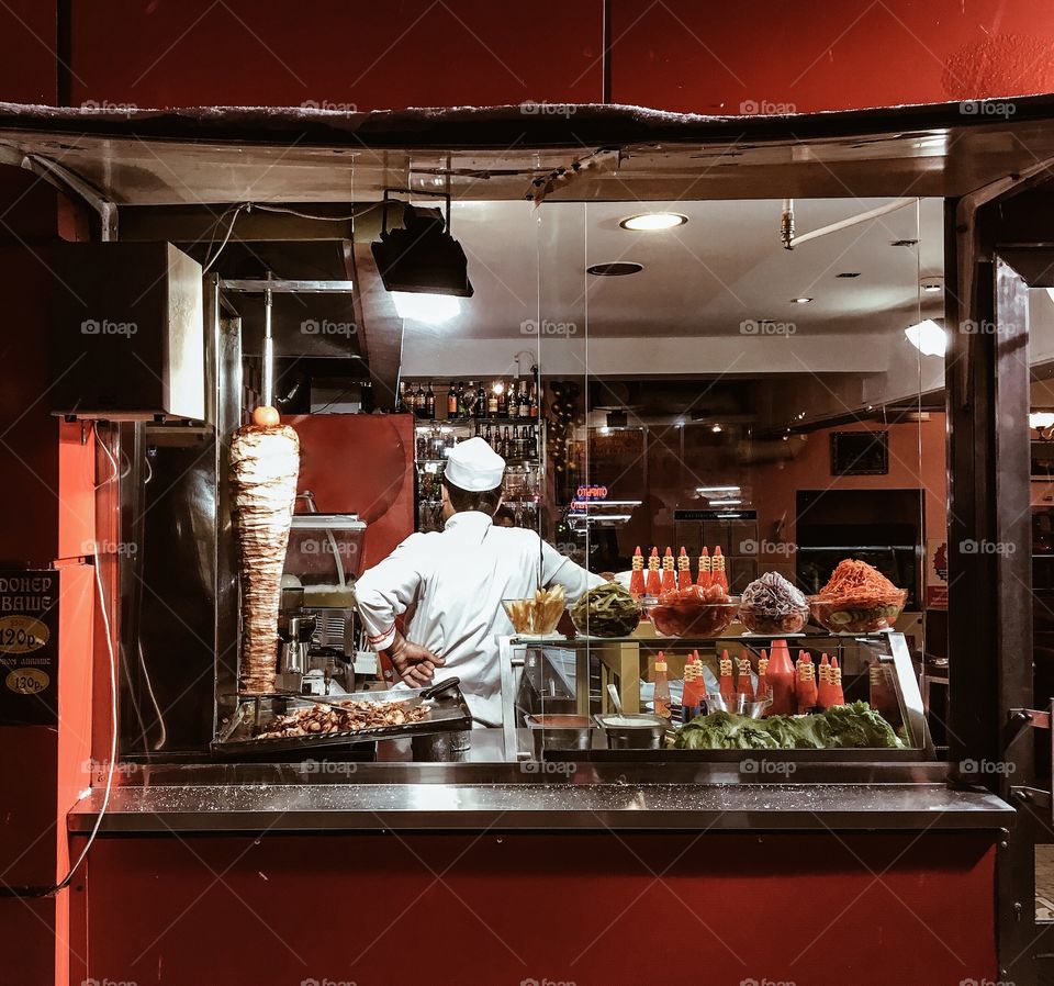 Street food cafe with turkish shawarma kebab and chef beyond the counter in evening light   