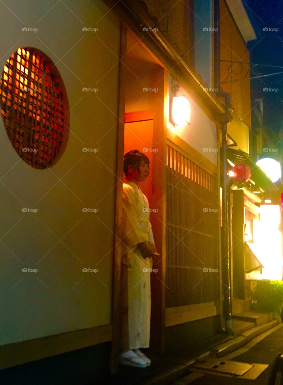 A girl stands quietly in a doorway along Kyoto's Pontocho Alley in Kyoto, Japan on a warm summer evening.