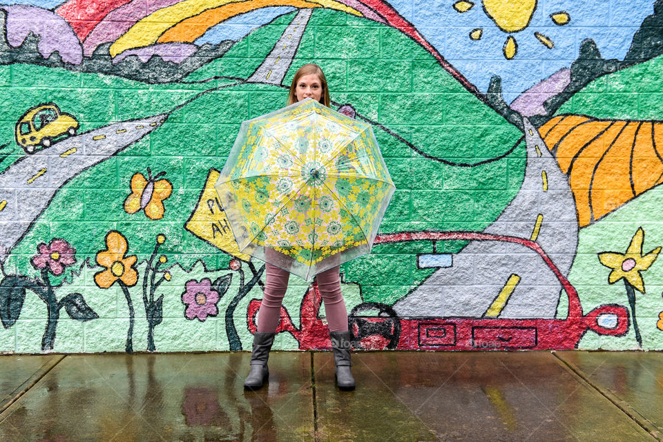 Young woman holding a colorful umbrella out in front of her with a colorful mural in the background