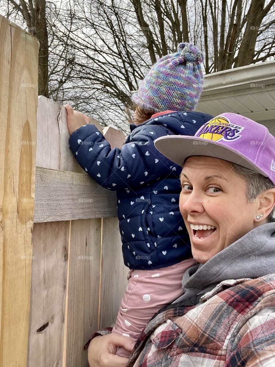 Surprising the neighbors by looking over the fence, mother lifts toddler to look over fence and surprise neighbors, neighborhood watch, Nosey Neighbor, little Nosey Neighbor, funny neighbor picture, looking over the fence and peeping at neighbors 