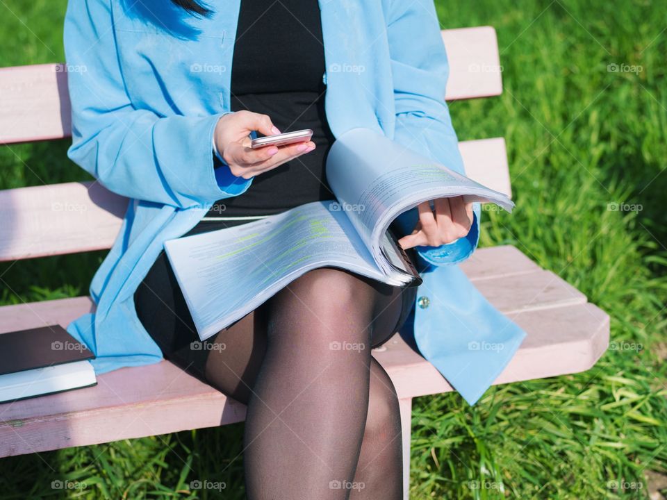 Business woman using her smartphone while sitting on the park bench 
