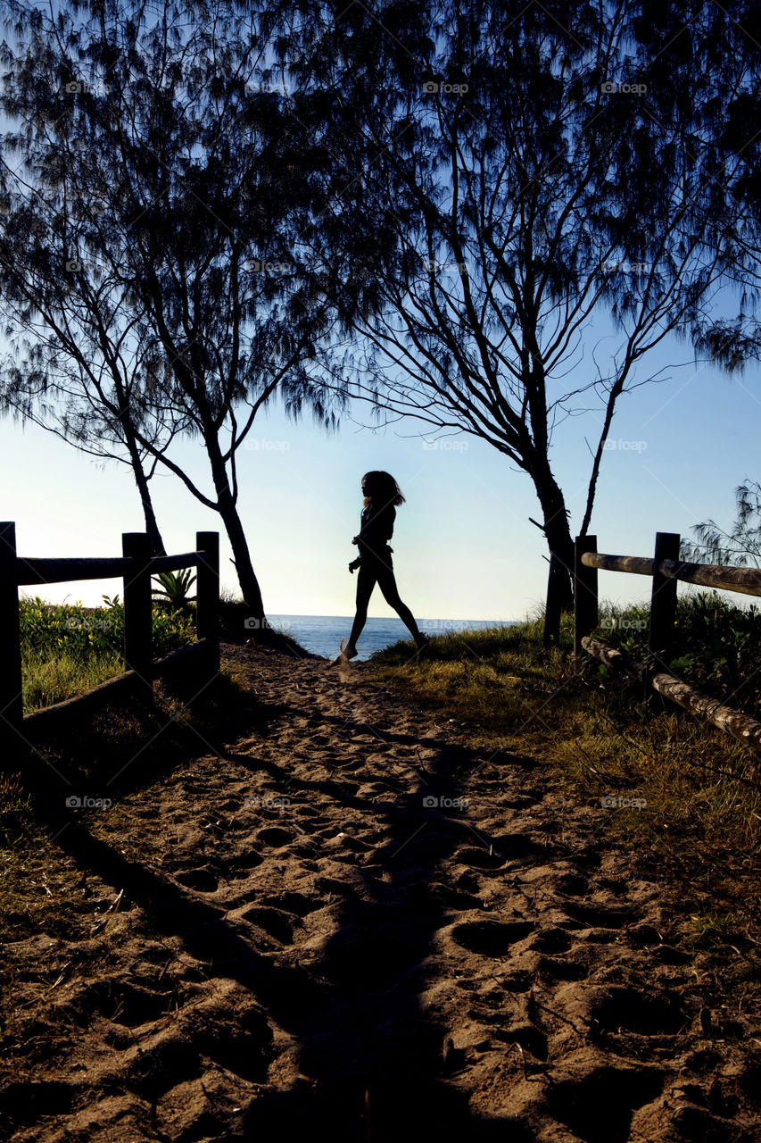 silhouette of a girl at the end of the trail, leaping off the sand, in between trees
