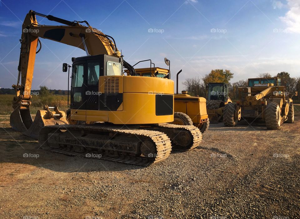Yellow excavating and earth moving equipment at a construction site including tracked and wheeled vehicles