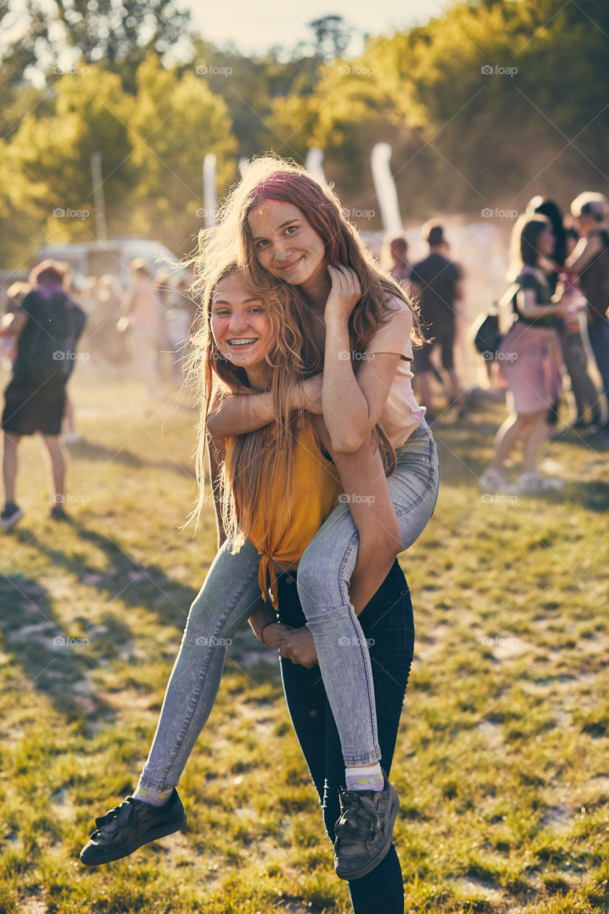 Portrait of happy smiling young girls with colorful paints on faces and clothes. Two friends spending time on holi color festival. Real people, authentic situations