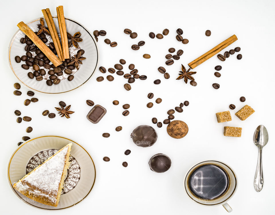 coffee beans are scattered on a white background, there is a cup of coffee, and plates with sweet