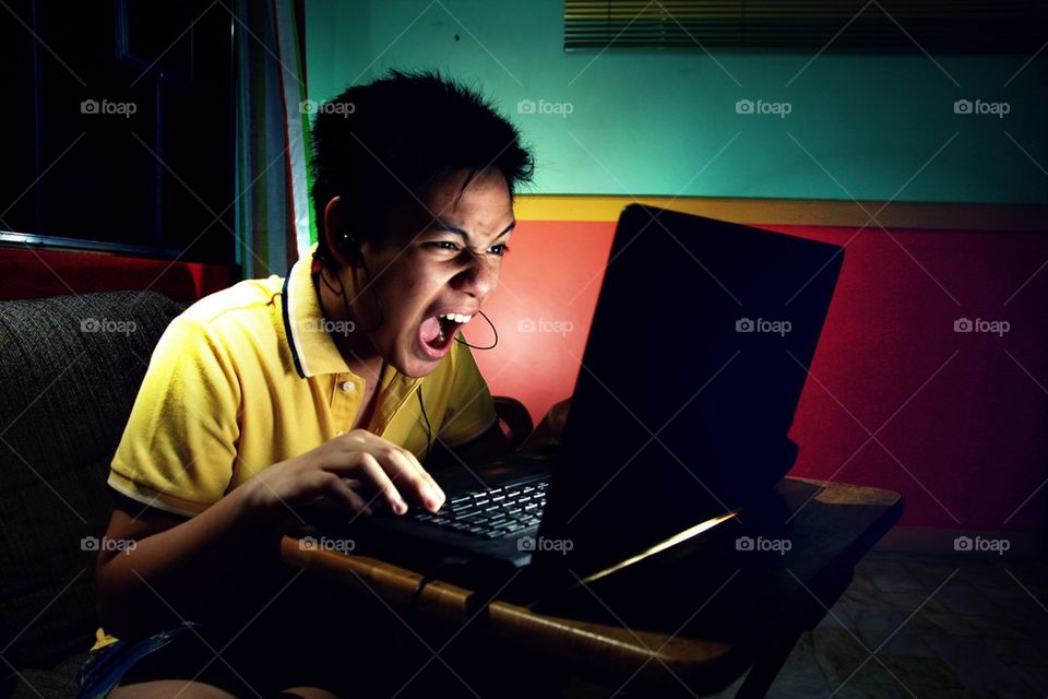 young asian teen intensely playing on a laptop computer