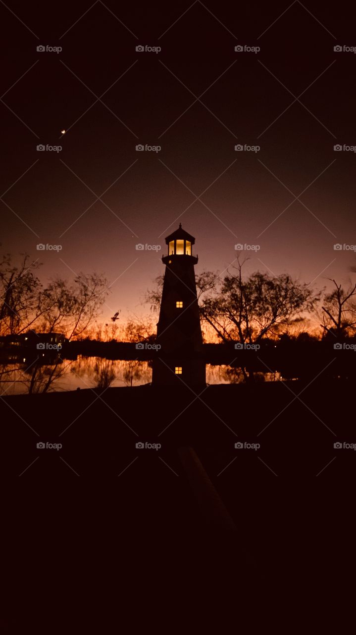 Mirrored Sunset Colors Silhouetted reflection on Lake Water Backlit to Lighthouse mixing with Night Colors. 