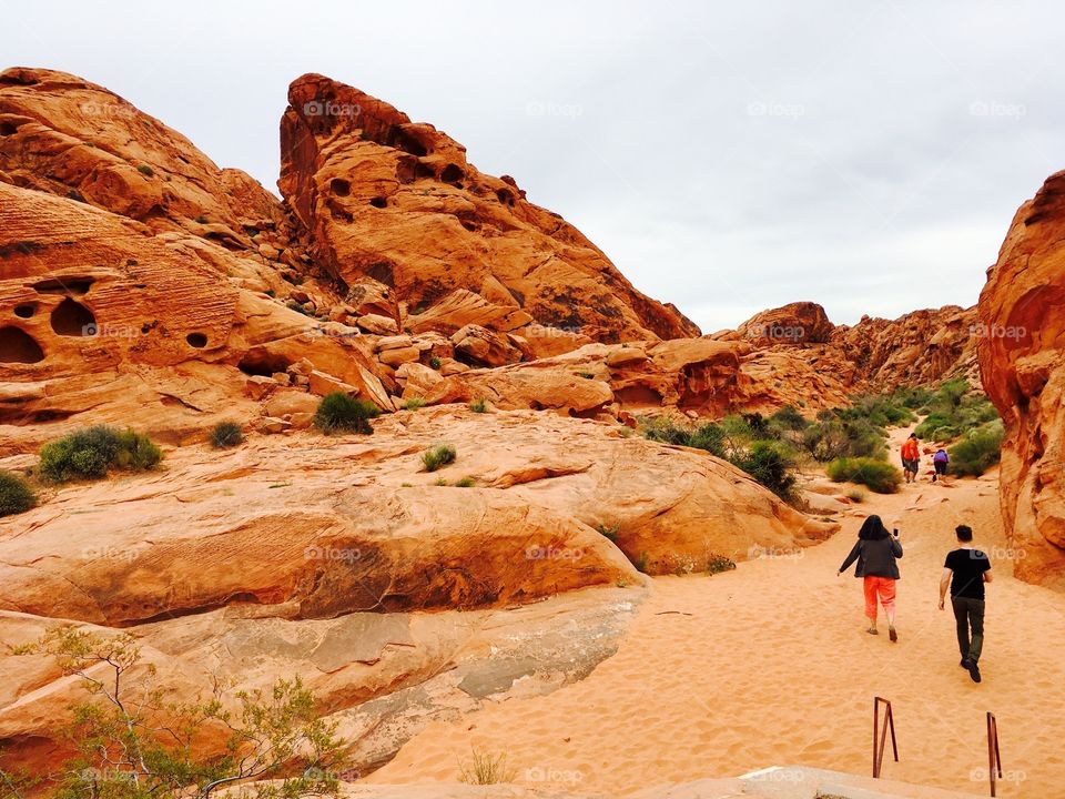 People traipse through the thick red sand in the Valley of Fire in Nevada. Massive red rock formations jut up all around them. 