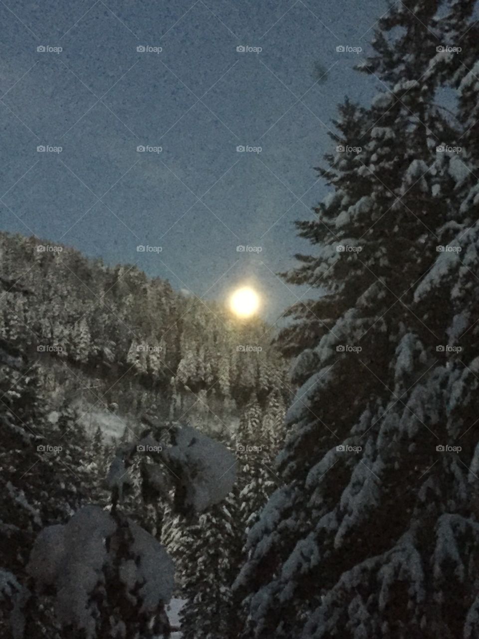 The full moon setting behind snow encased mountain top 