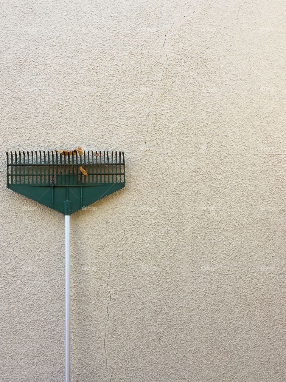 Green garden rake leaning up against cracked stucco exterior wall minimalist negative space and room
For text 