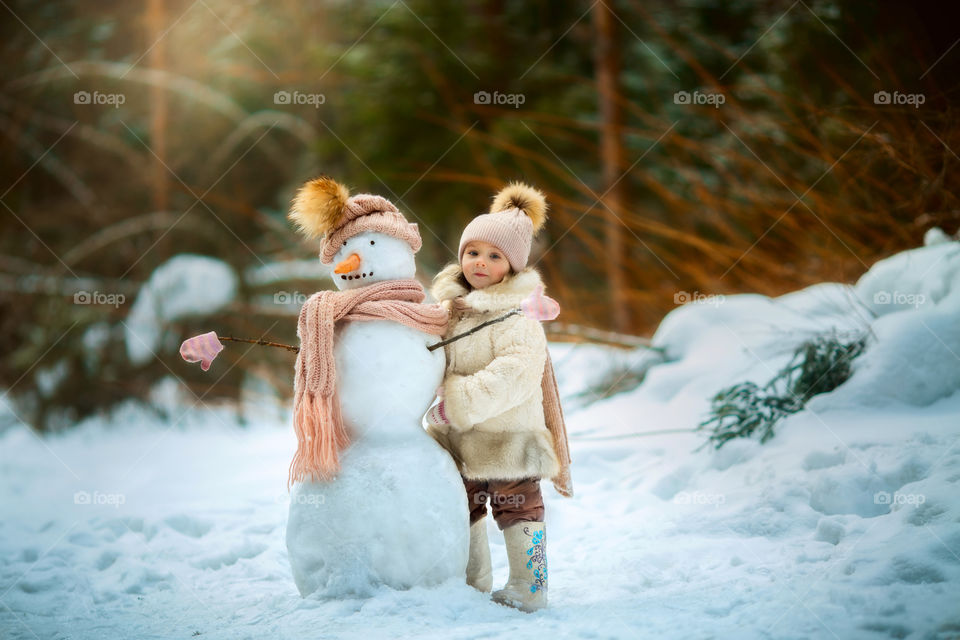 Little girl with snowman in winter forest at sunny day