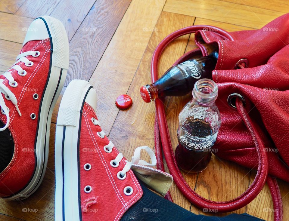 Coca Cola bottles on hardwood floor with red sneakers and red leather bag.