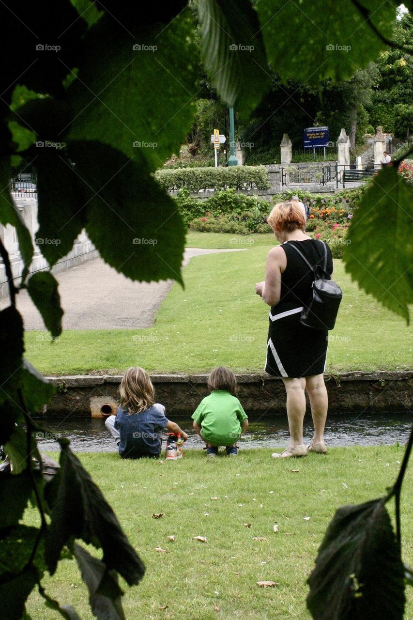 Two kids and a woman near the water stream at the city park 