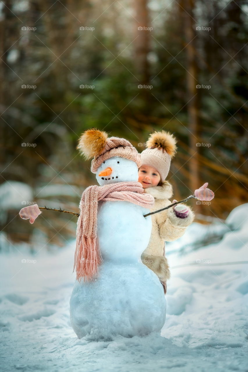 Little girl with snowman in winter park