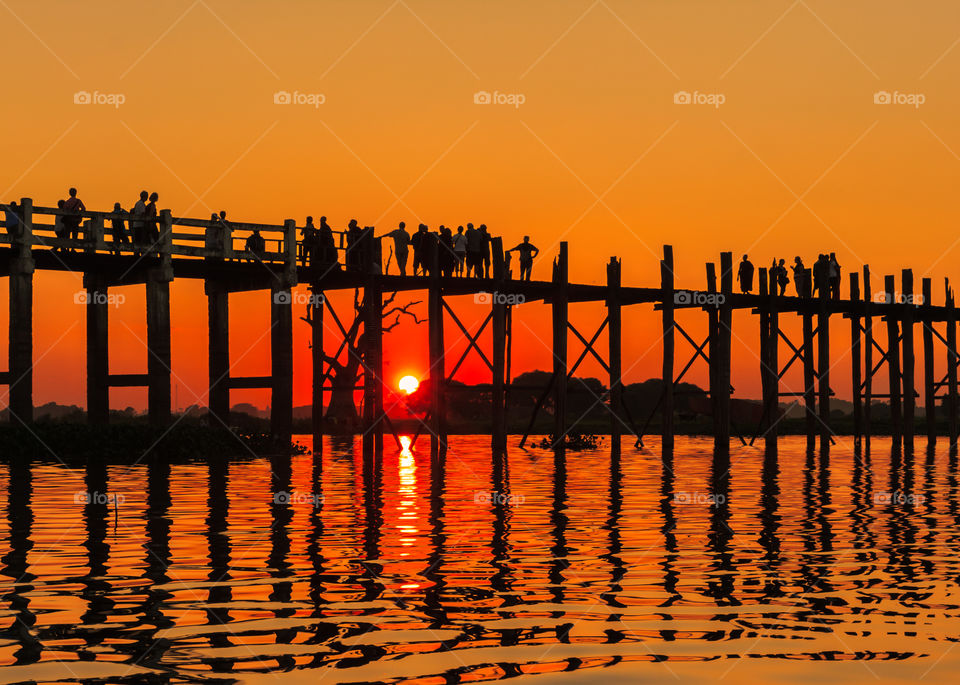 People crossing lake on bridge. People crossing lake on wooden bridge at golden hour in Myanmar