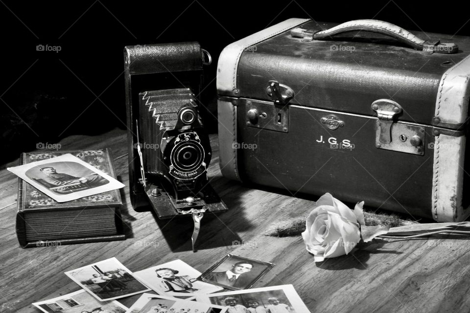 Black and white still life of old camera and old photographs beside an old piece of luggage