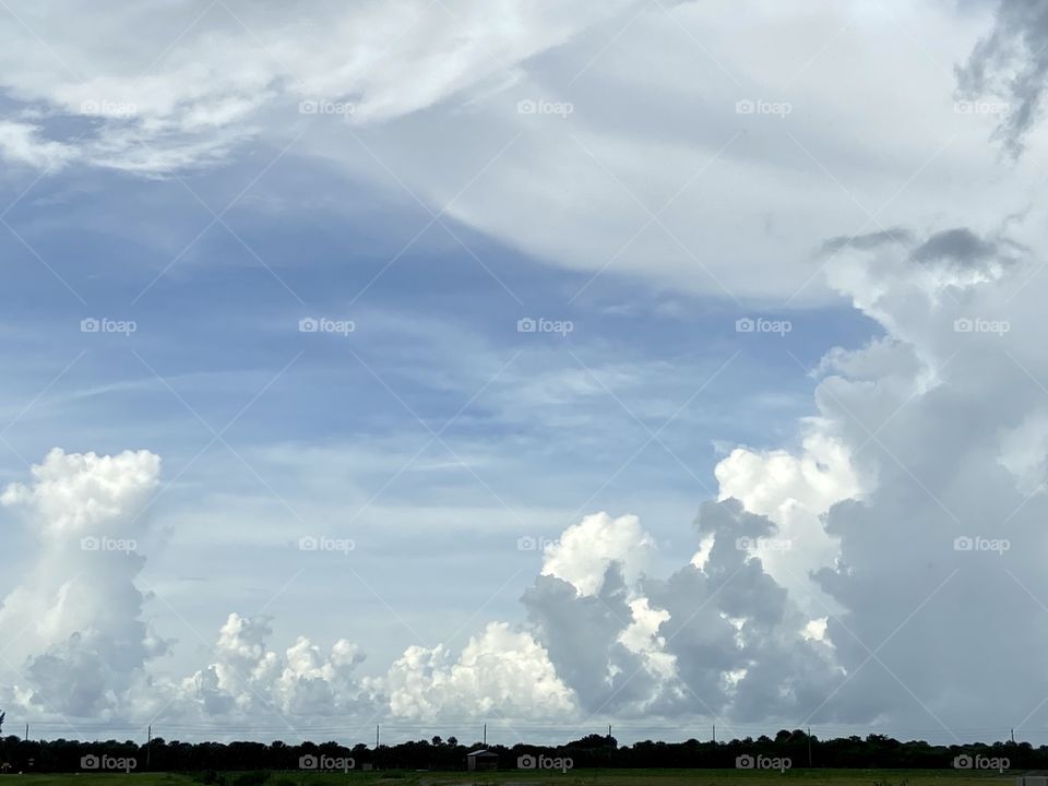A blue sky with puffy white and dark grey clouds above a green countryside