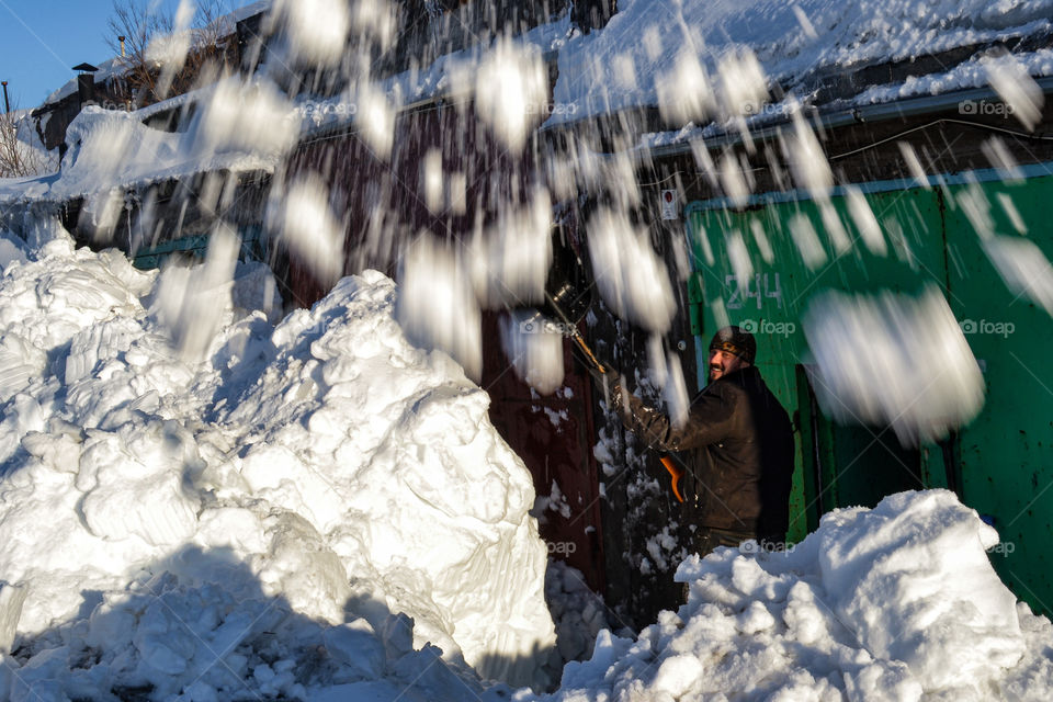 a smiling man in a good mood digs up a garage from the snow, snow flies right into the camera
